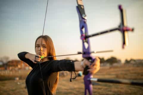 One teenage girl practicing archery outdoors at sunset on the field.