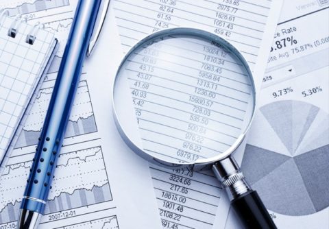 magnifying glass and pen sitting on financial documents