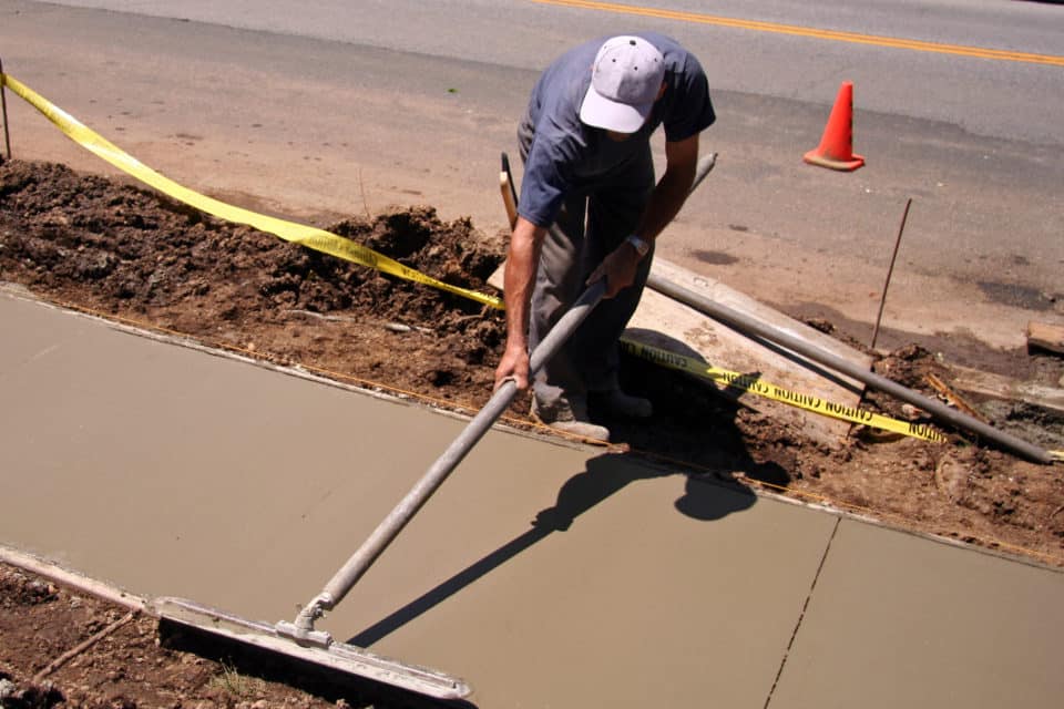 Construction worker smoothing out newly poured concrete sidewalk