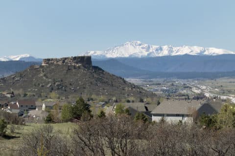 Castle Rock mesa and homes stand in front of a snow covered Pikes Peak with Interstate 25 winding its way to the snowy Rocky Mountains, Castle Rock, Colorado.