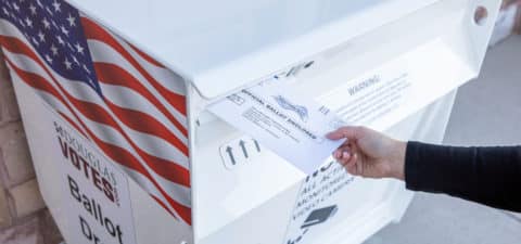 Photo of a person putting their ballot in a drop box