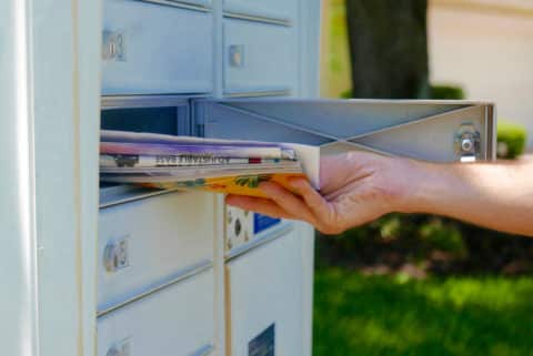 Person's hand pulling a pile of junk mail out of a community mailbox