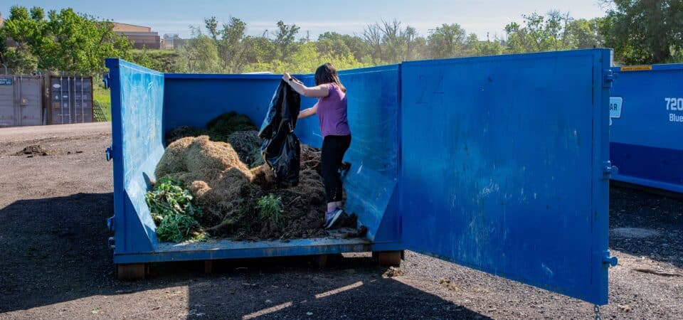 Woman using green yard waste dumpster