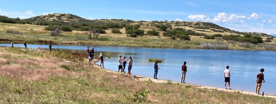 Young adults fishing from the shore of a lake.